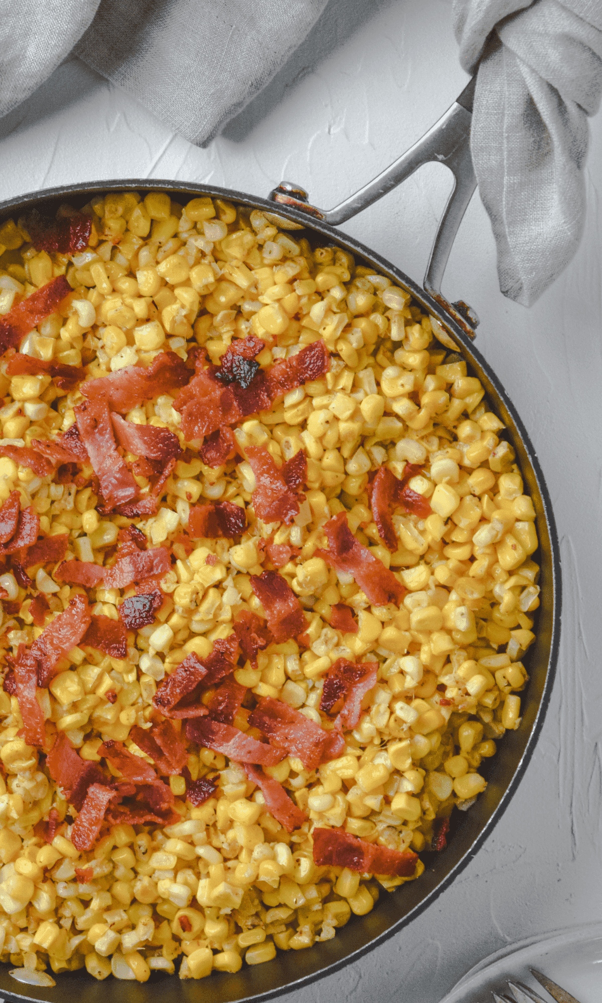 Sweet corn topped with bacon in a skillet. 