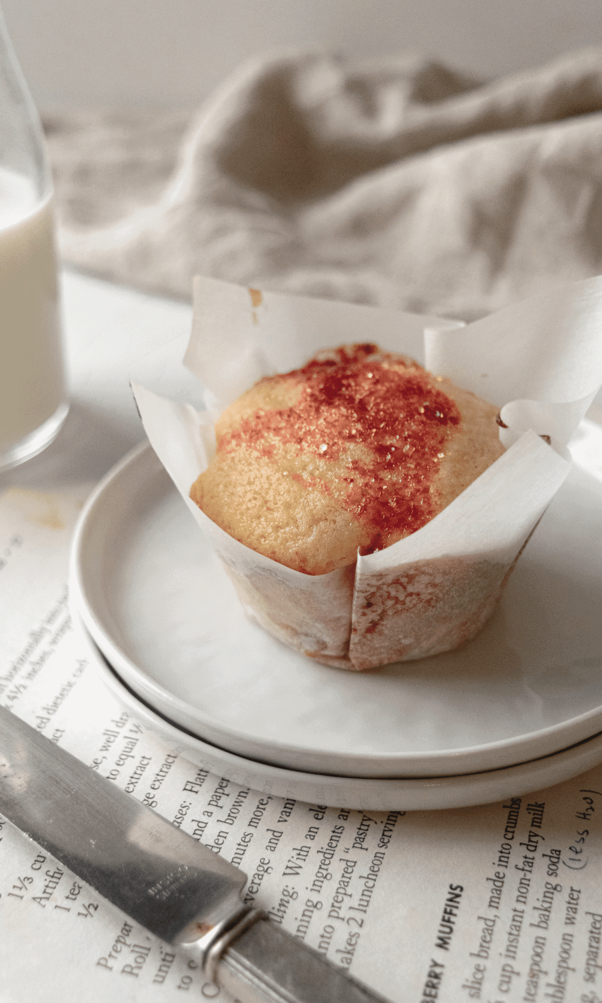 A Strawberry Cream Cheese Muffin in a parchment paper liner on a white plate.