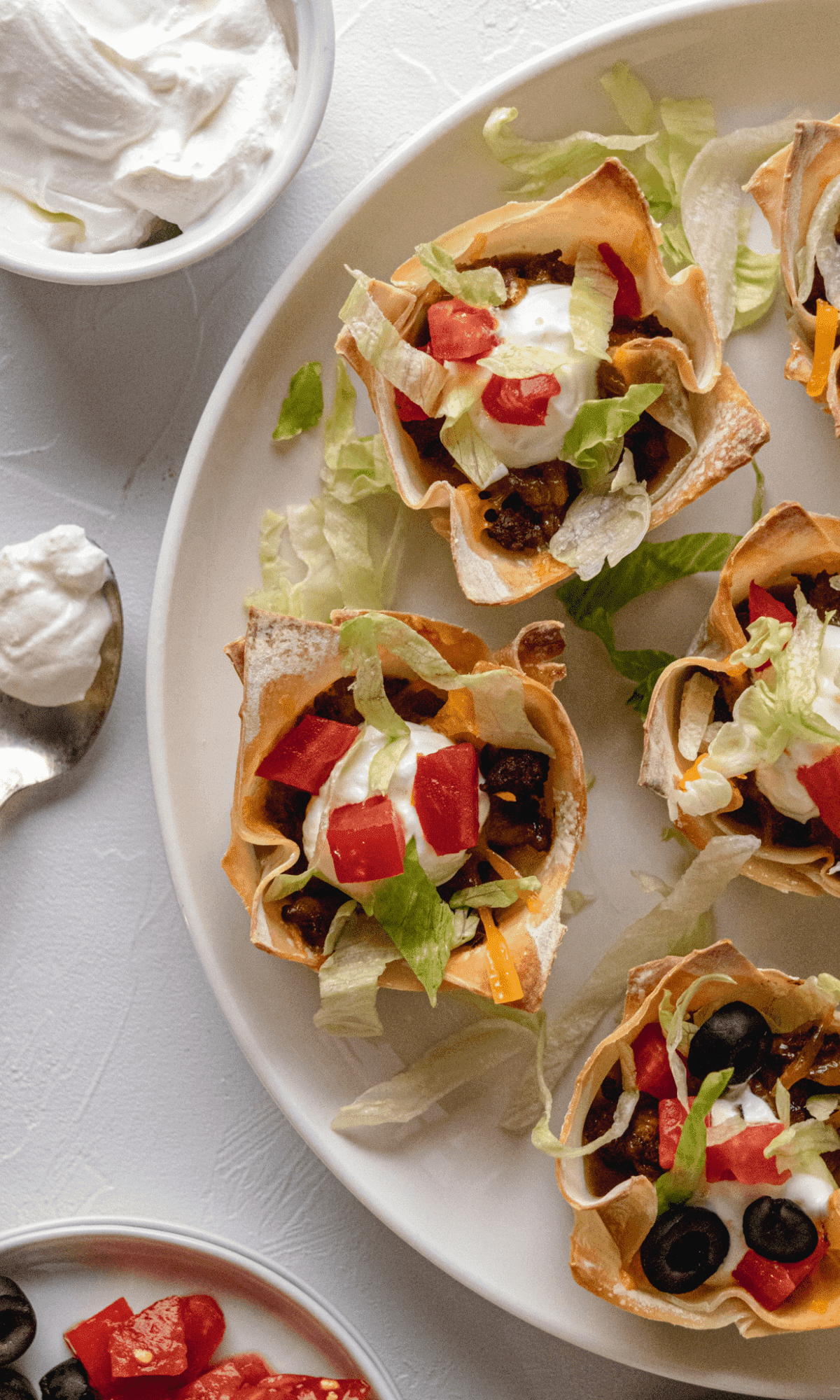 Overhead shot of Double Layer Beef Taco Cups on a white plate with a spoonful of sour cream next to it.
