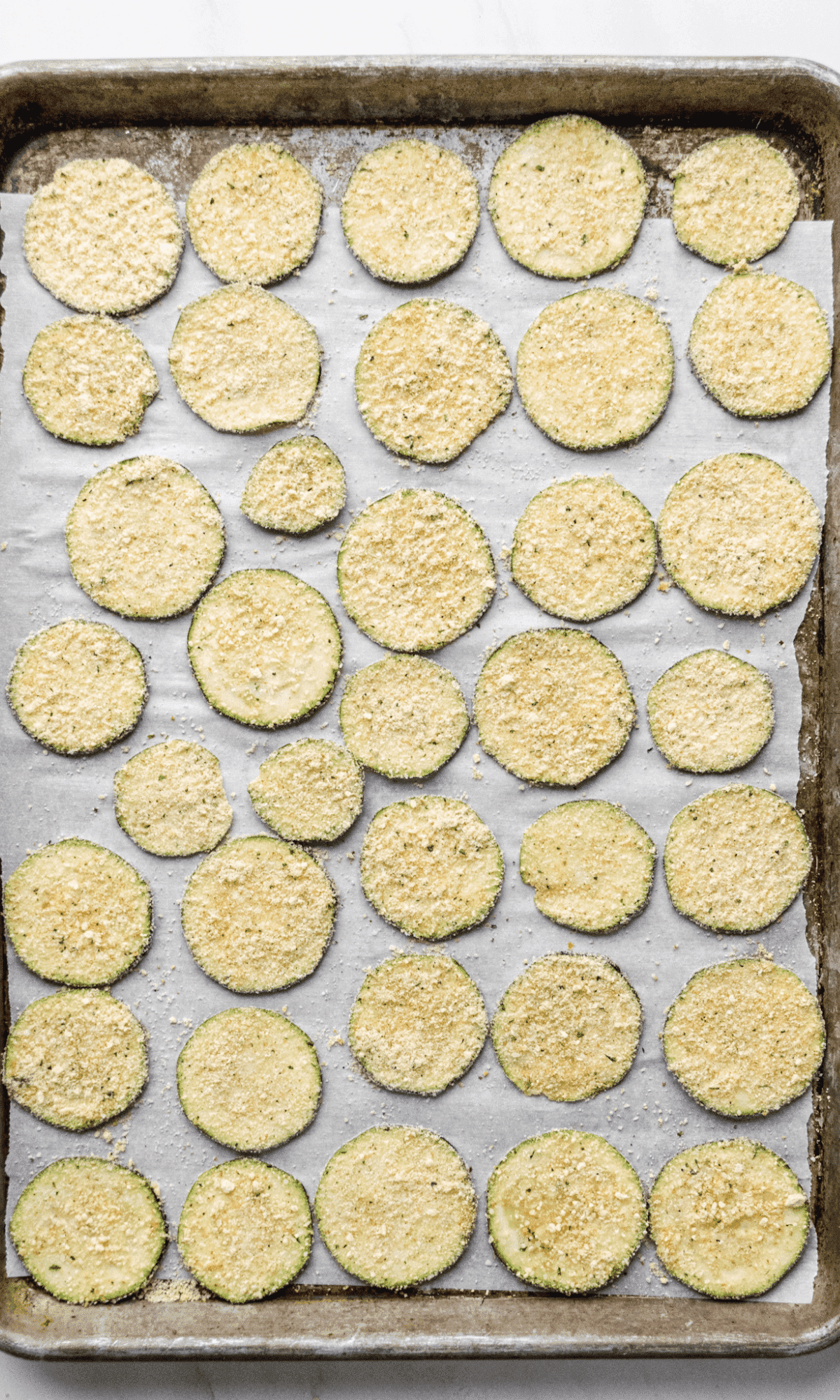 Overhead shot of breaded zucchini chips on a baking sheet.