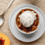 Overhead shot of peach crisp in a white ramekin topped with a scoop of vanilla ice ceam.
