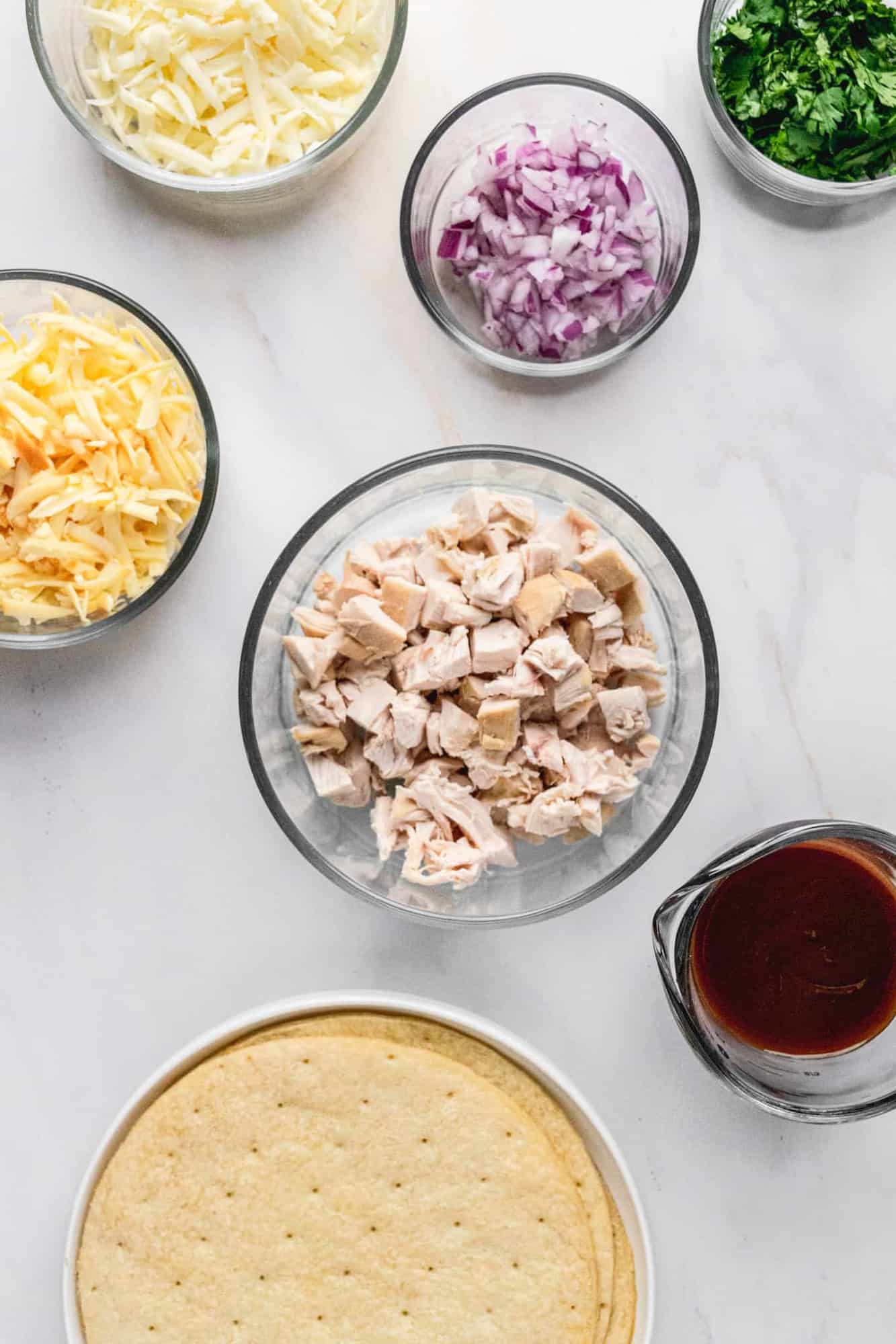 Ingredients for BBQ Chicken Pizza in varying bowl and plate sizes.