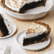 Piece of S'mores Fudge Pie on white plate with whole pie behind it.
