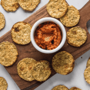 Overhead shot of zucchini chips on a wooden cutting board with tomato dipping sauce.