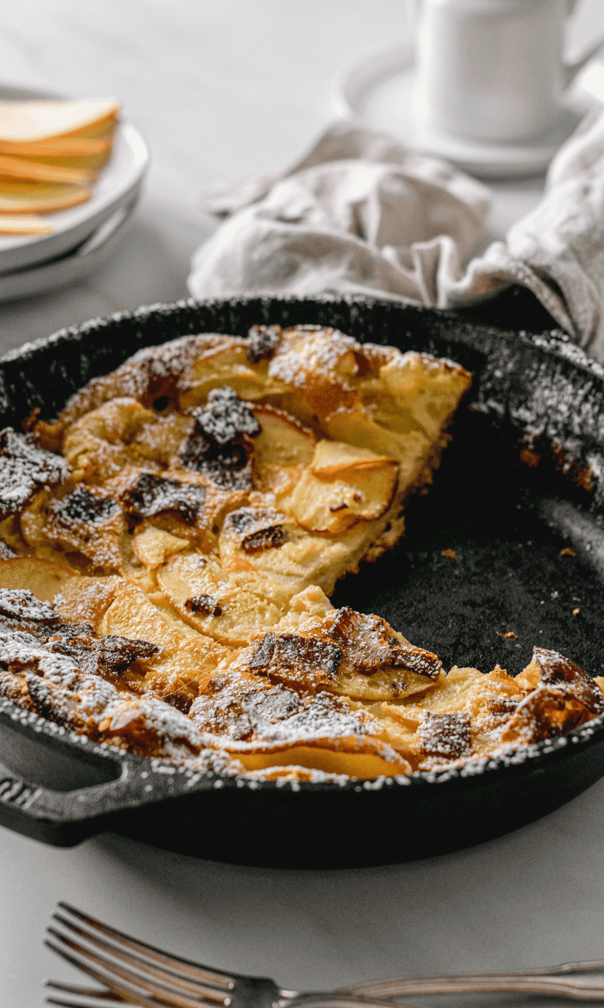 Bacon Apple Dutch Baby in a cast iron skillet with a slice missing.