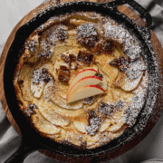 Overhead shot of Bacon Apple Dutch Baby in cast iron skillet topped with dusting of powdered sugar.