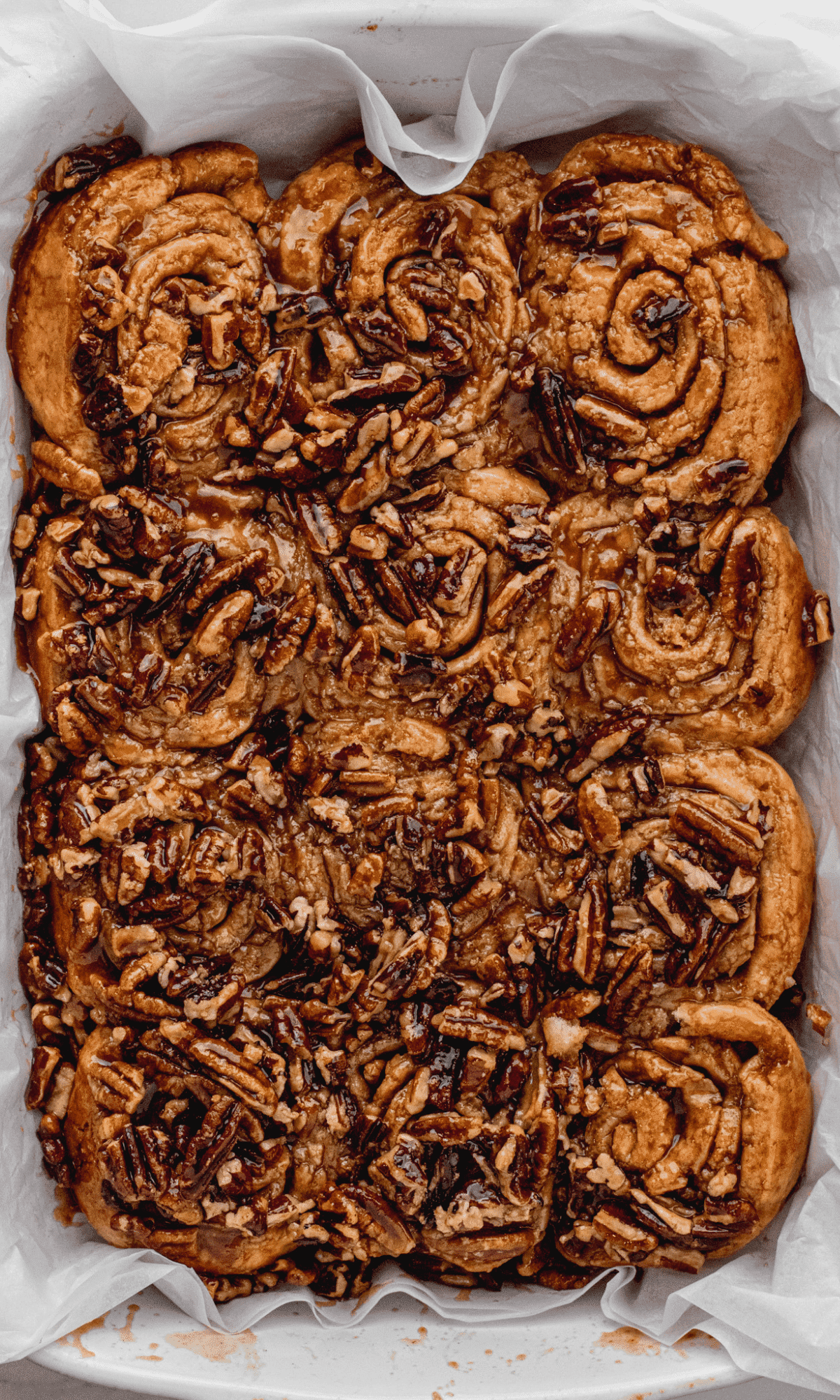 Caramel Pecan Sticky Buns in white pan on white parchment paper.