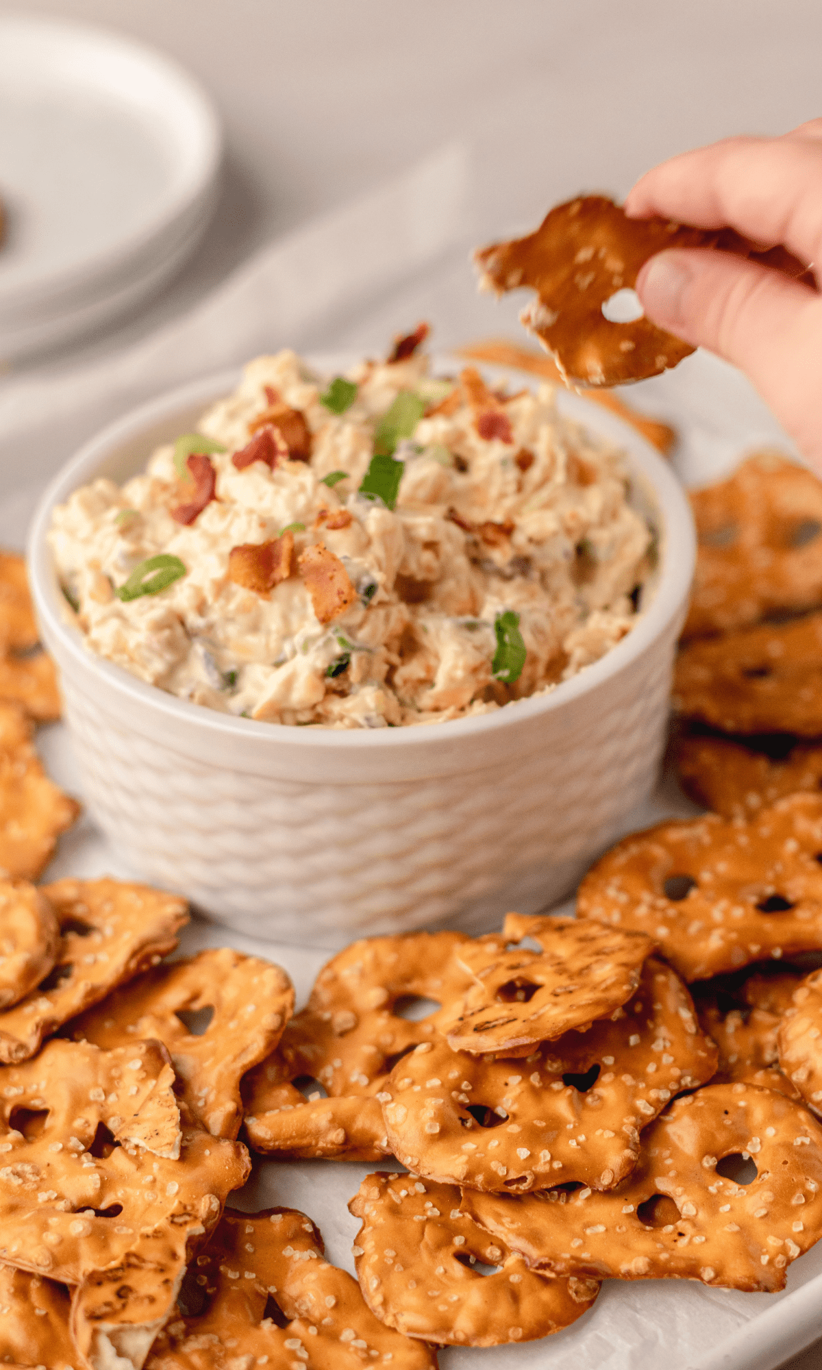 Pretzel Dip in a small white bowl surrounded by pretzel crisps and a tiny hand dipping a pretzel crisp in the dip.