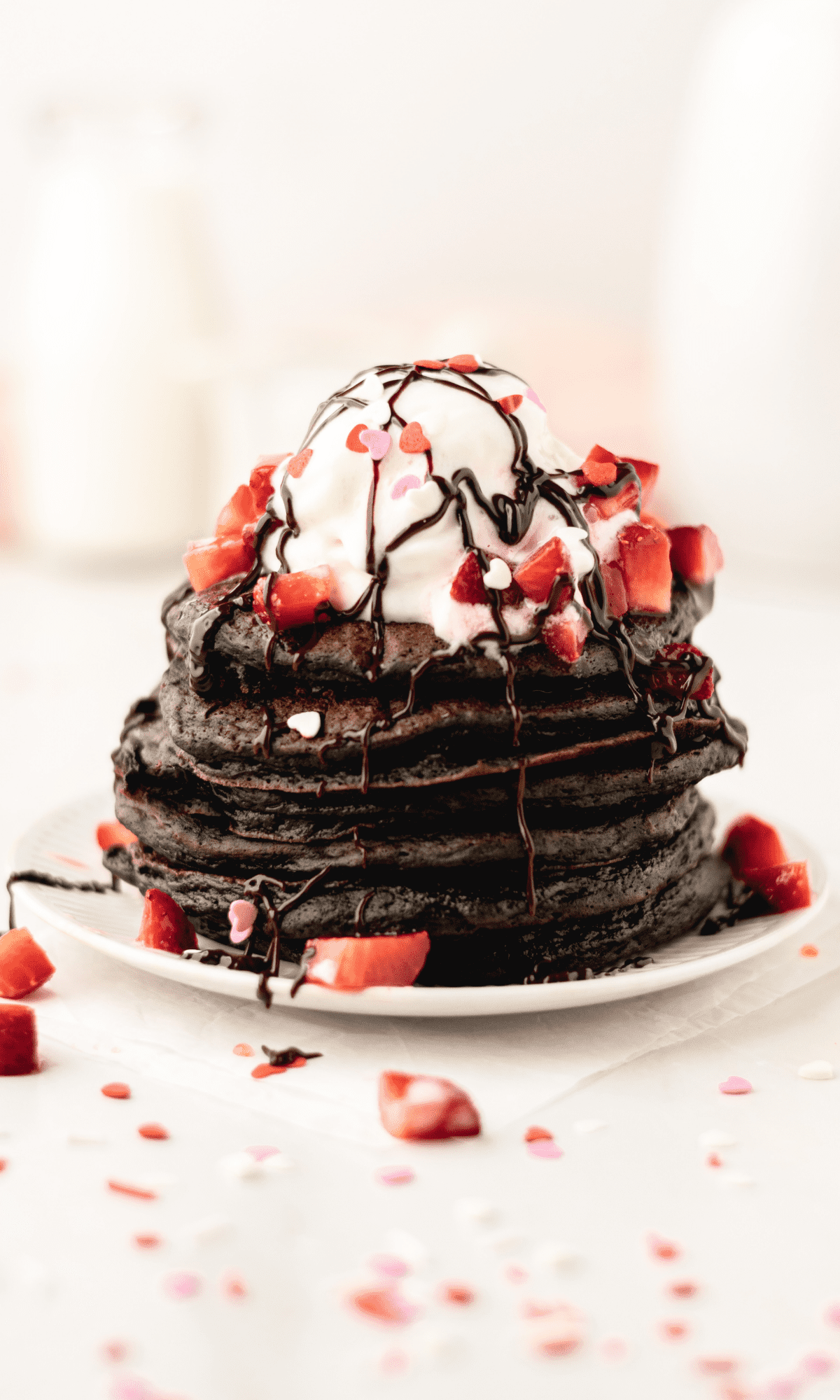 Straight on shot of a stack of chocolate buttermilk pancakes with whipped cream, strawberries, chocolate sauce and Valentine sprinkles.
