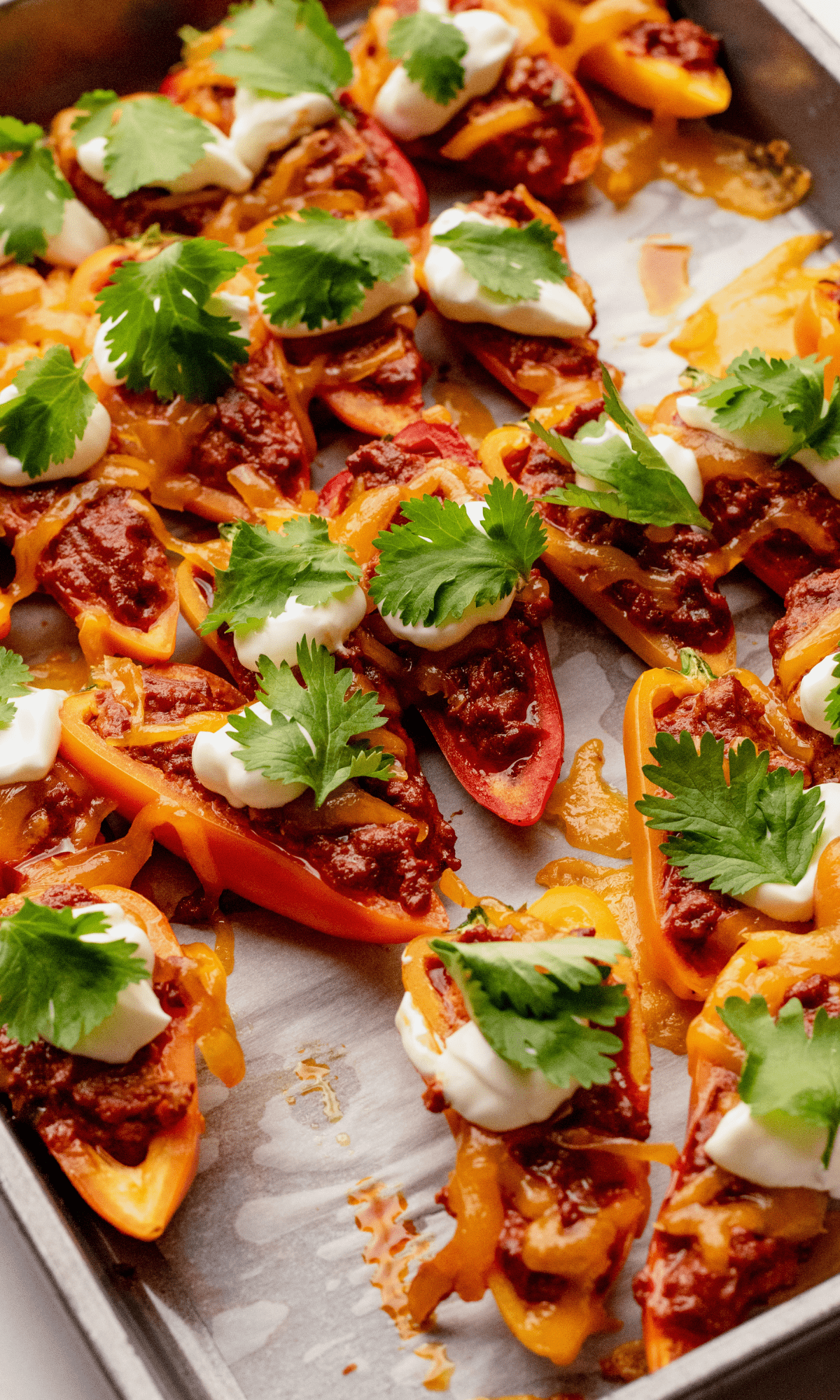 Mini Bell Pepper Nachos on a sheet pan with dollops of sour cream and cilantro.