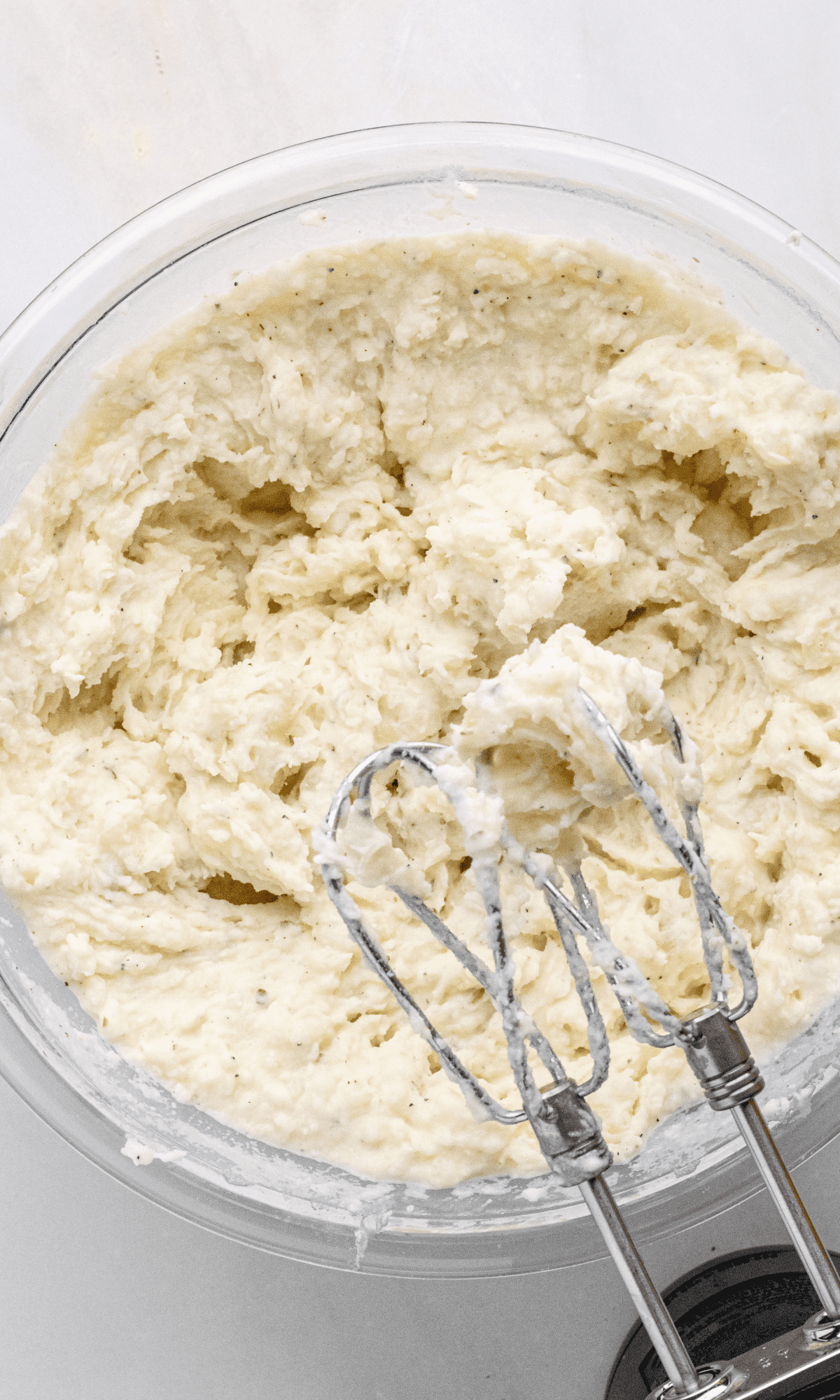 Overhead shot of Boursin Mashed Potatoes in a glass bowl after being mixed with a hand mixer.