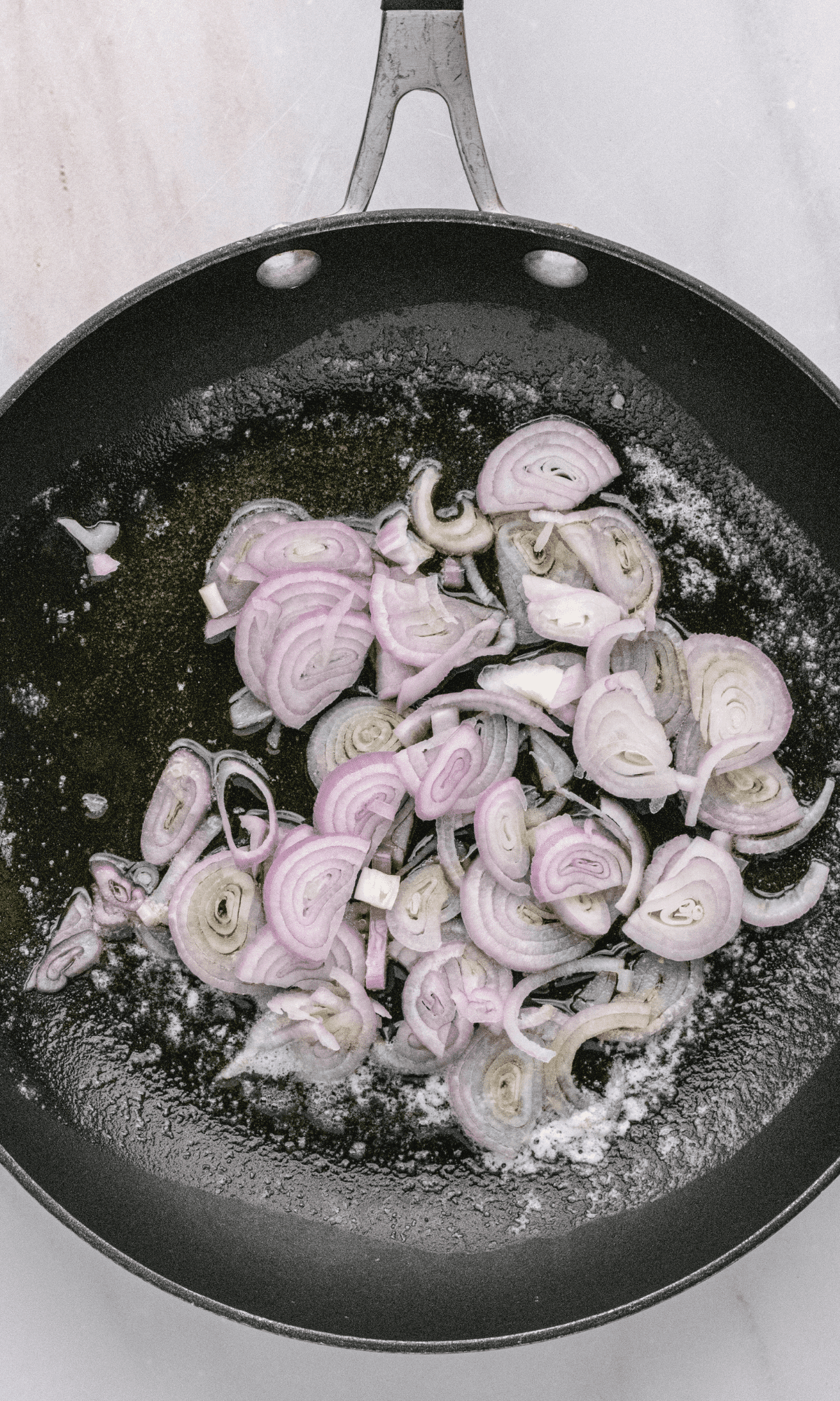 Overhead shot of sliced shallots in frying pan with melted butter and olive oil.