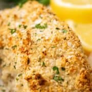 Crunchy Baked Cod with Parmesan Panko Breadcrumbs on white parchment paper surrounded by potatoes, lemon wedges and green beans.