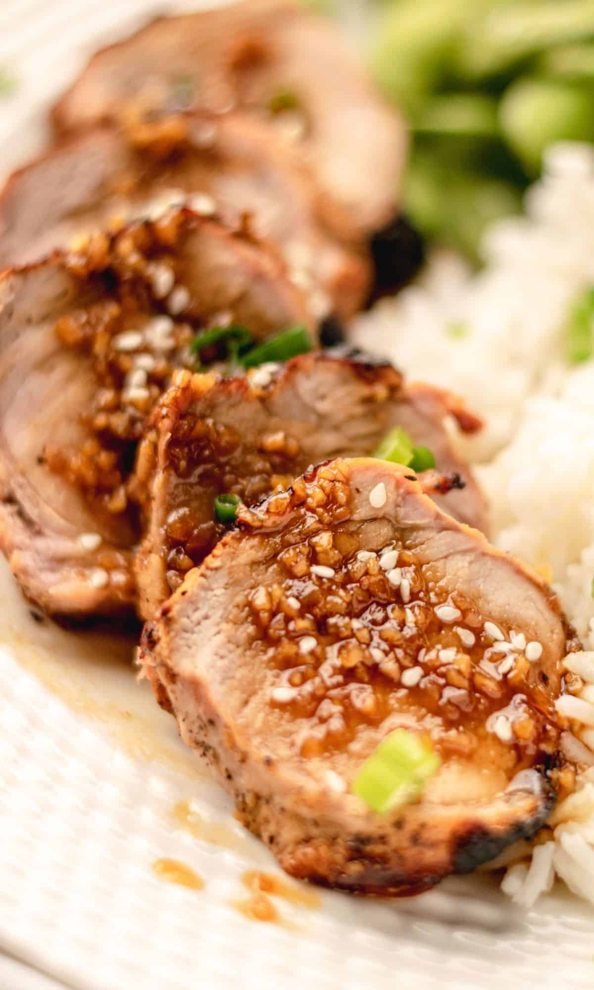 Pork tenderloin with a honey garlic sauce on a white plate with rice and edamame on the side.