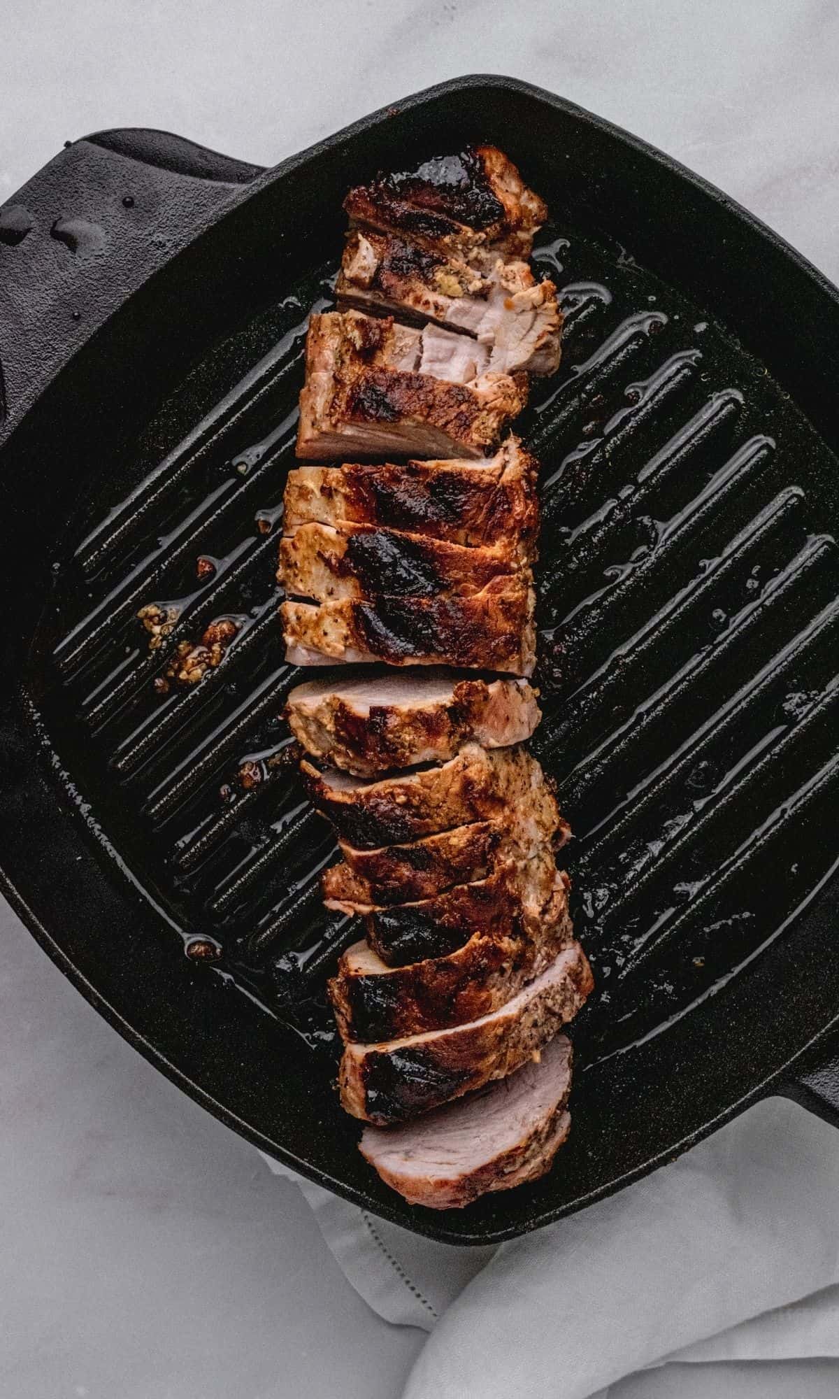 Sliced pork tenderloin in a cast iron skillet after resting.