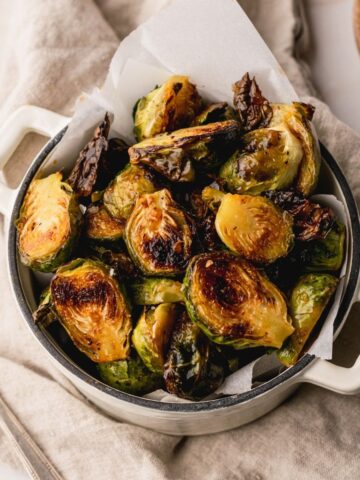 Honey Sriracha Brussels Sprouts in a small white dutch oven lined with white parchment paper.