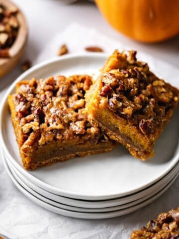 Two Pecan Pumpkin Pie Bars on a stack of small white plates.