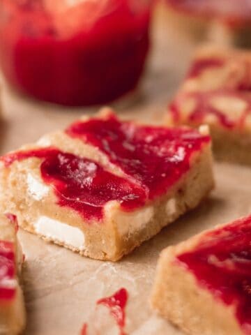 A stack of raspberry and White Chocolate Blondies on brown parchment paper.