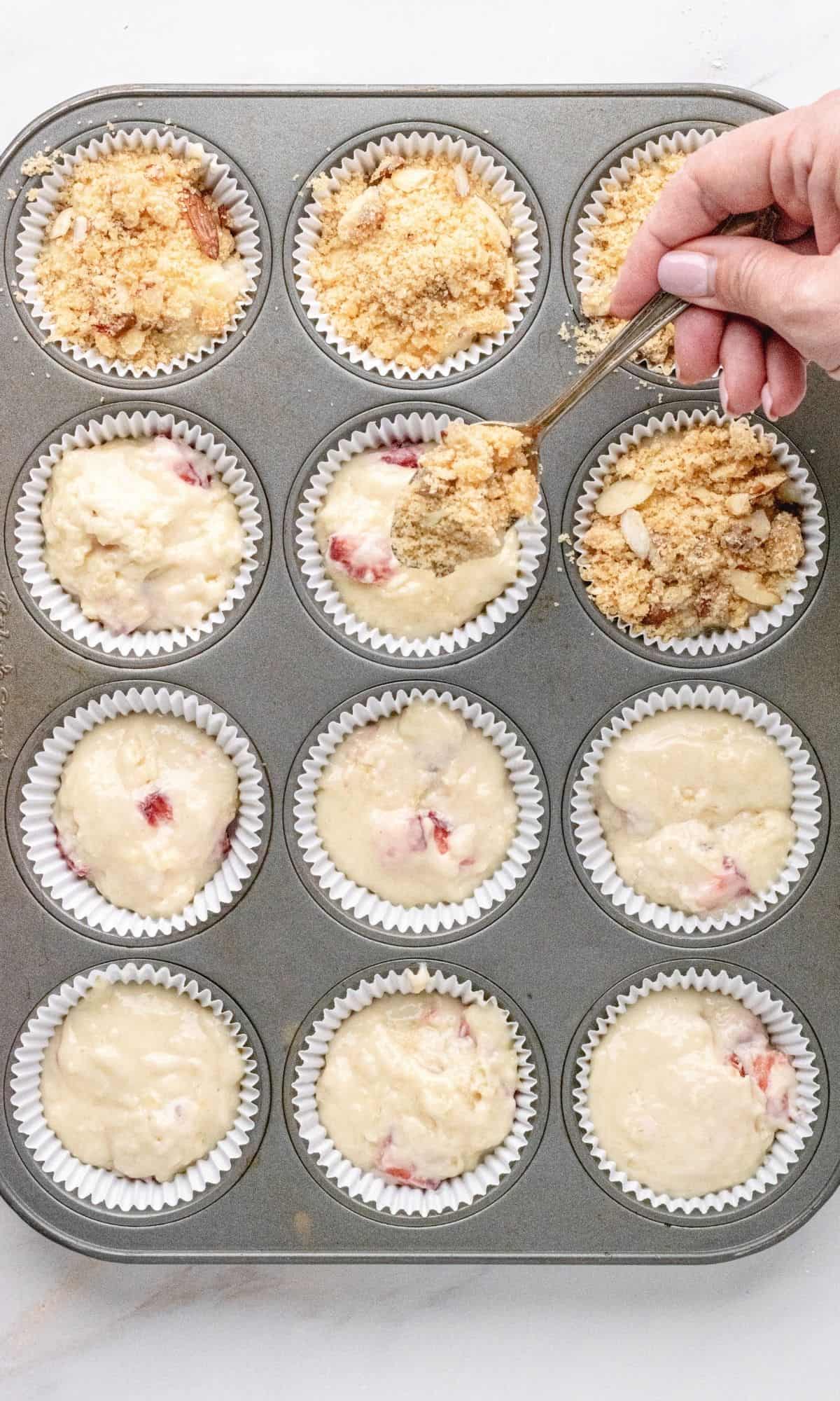 Crumb topping being spooned onto strawberry lemon muffin batter.