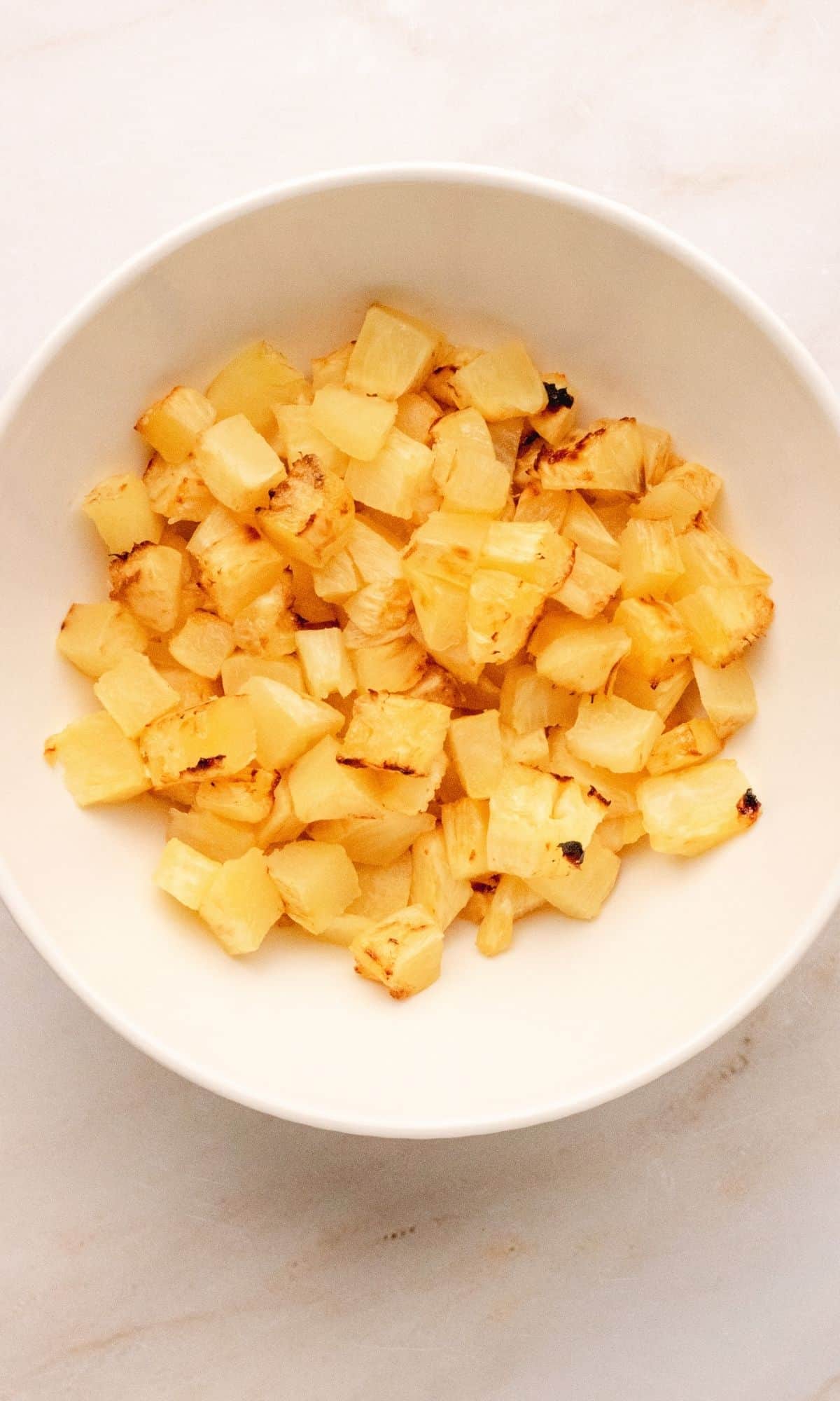 Chopped roasted pineapple in a white bowl.