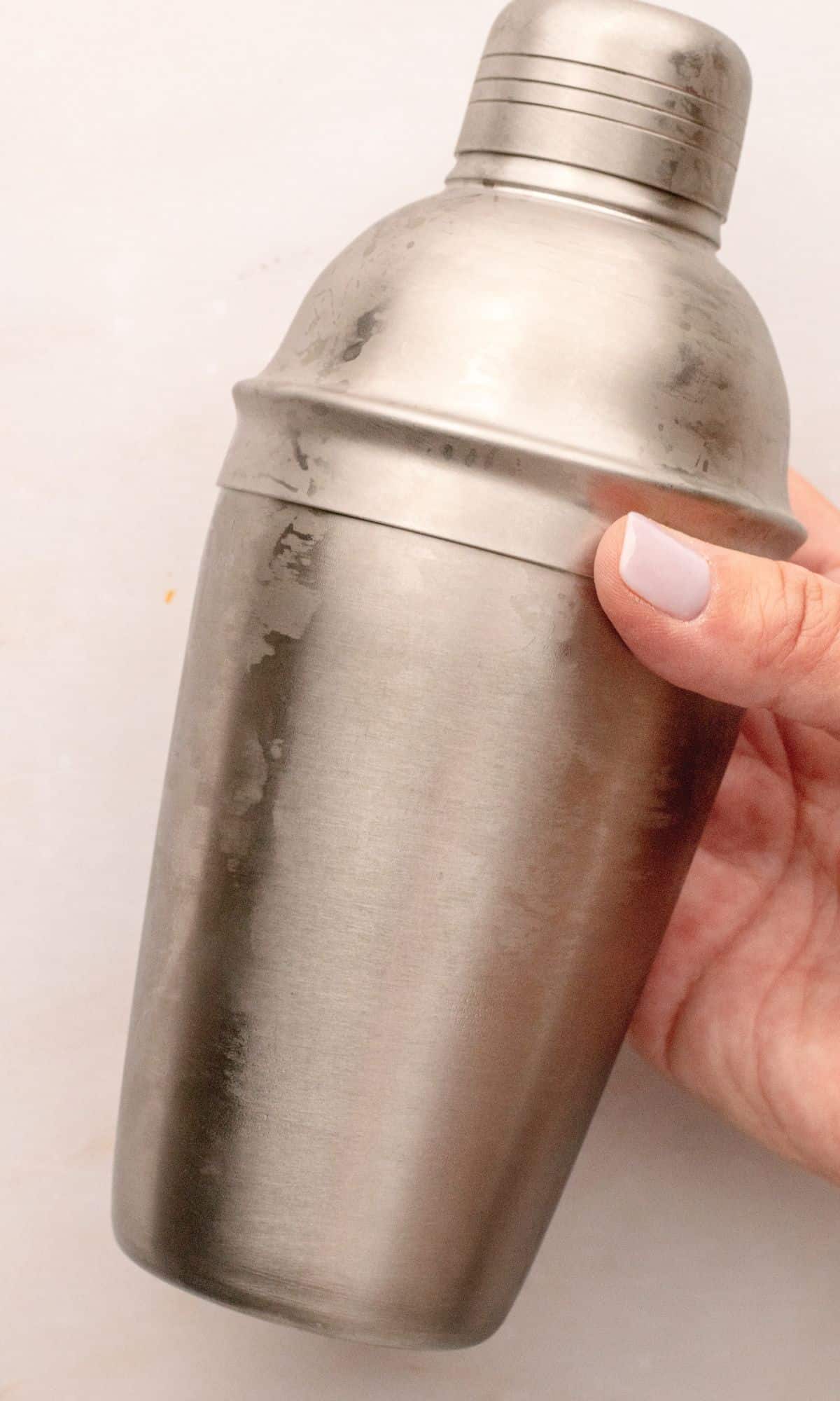 Metal cocktail shaker held in hand with condensation.