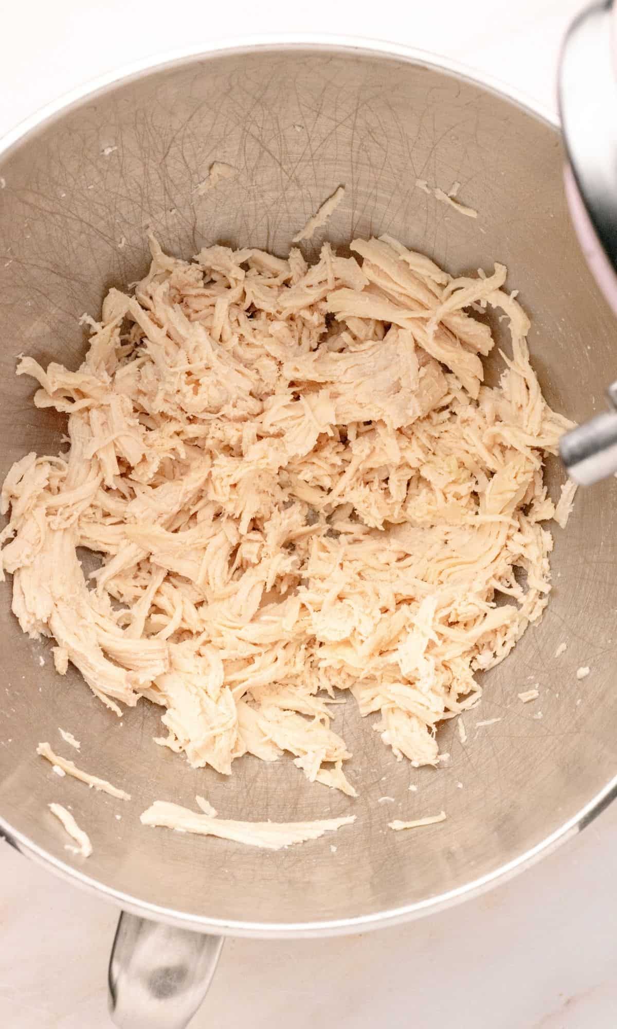 Shredded chicken in the bowl of a stand mixer.