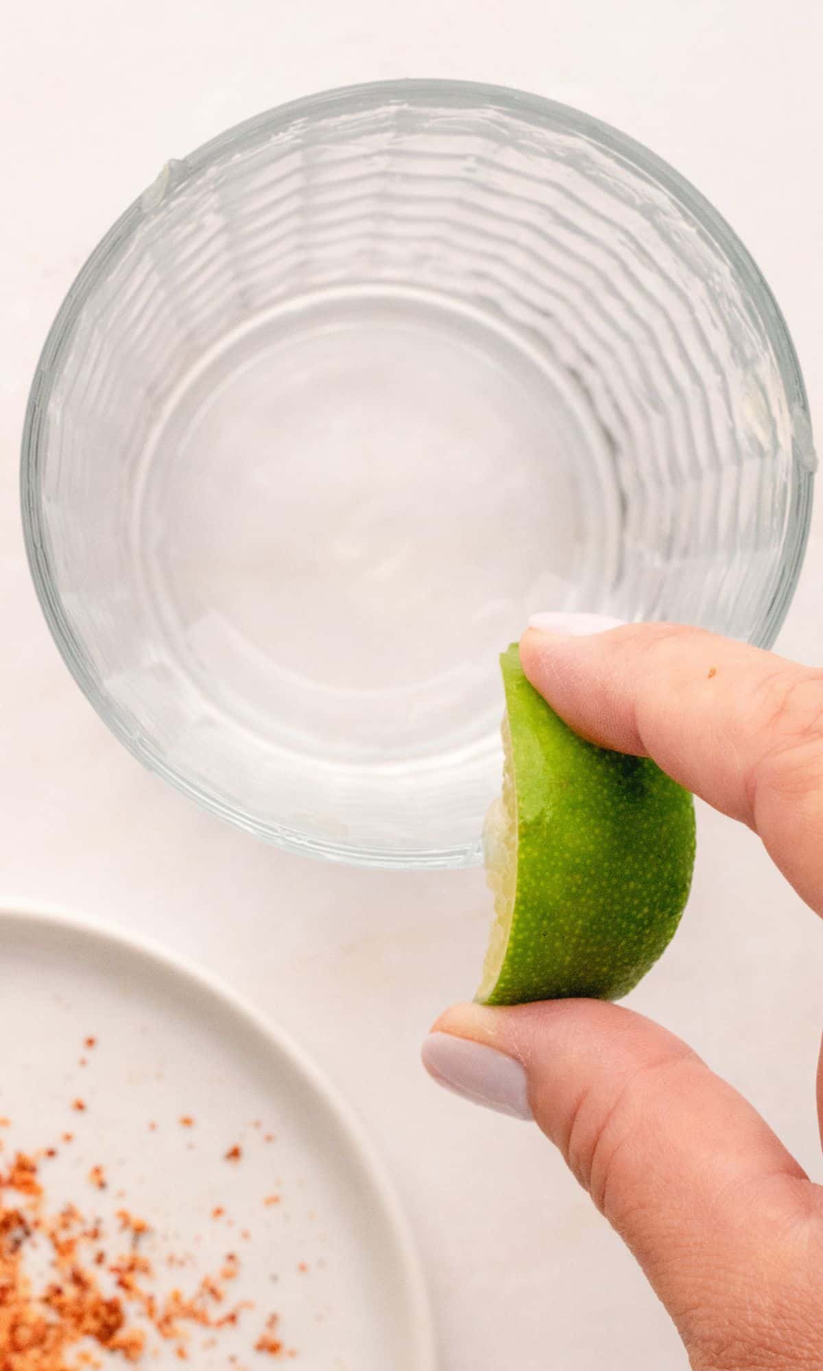 A lime wedge being rubbed on the rim of a glass.