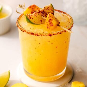 Hot honey spicy mango margartita in a glass with a mango and lime garnish.