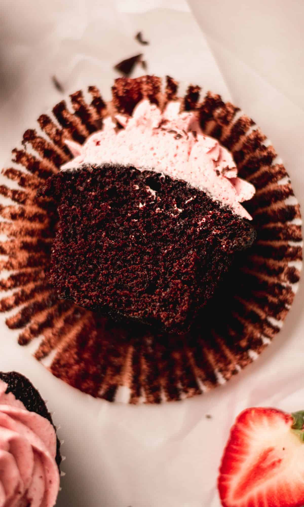 A cross section shot of a halved chocolate cupcake with strawberry buttercream frosting.