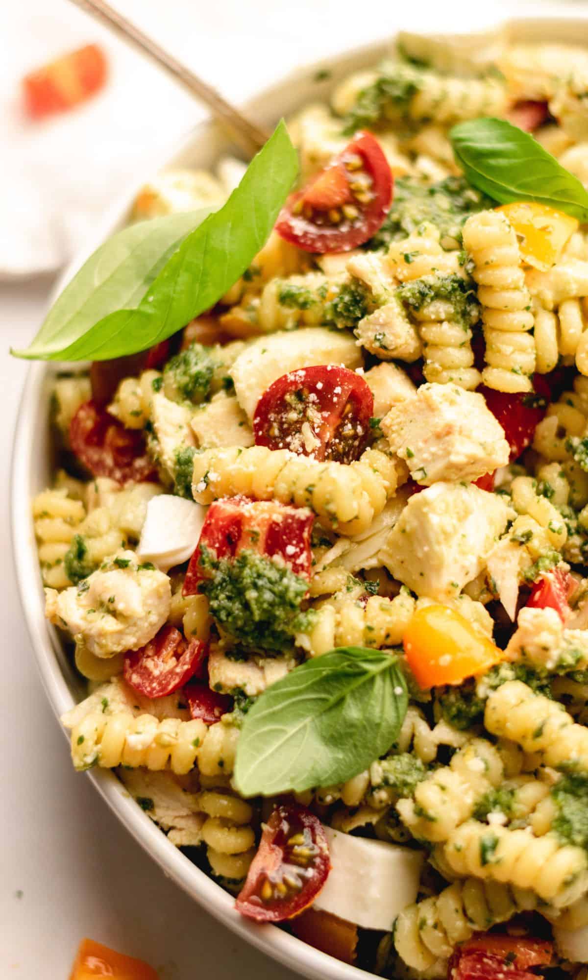 Pesto pasta salad topped with basil leaves in a white bowl.