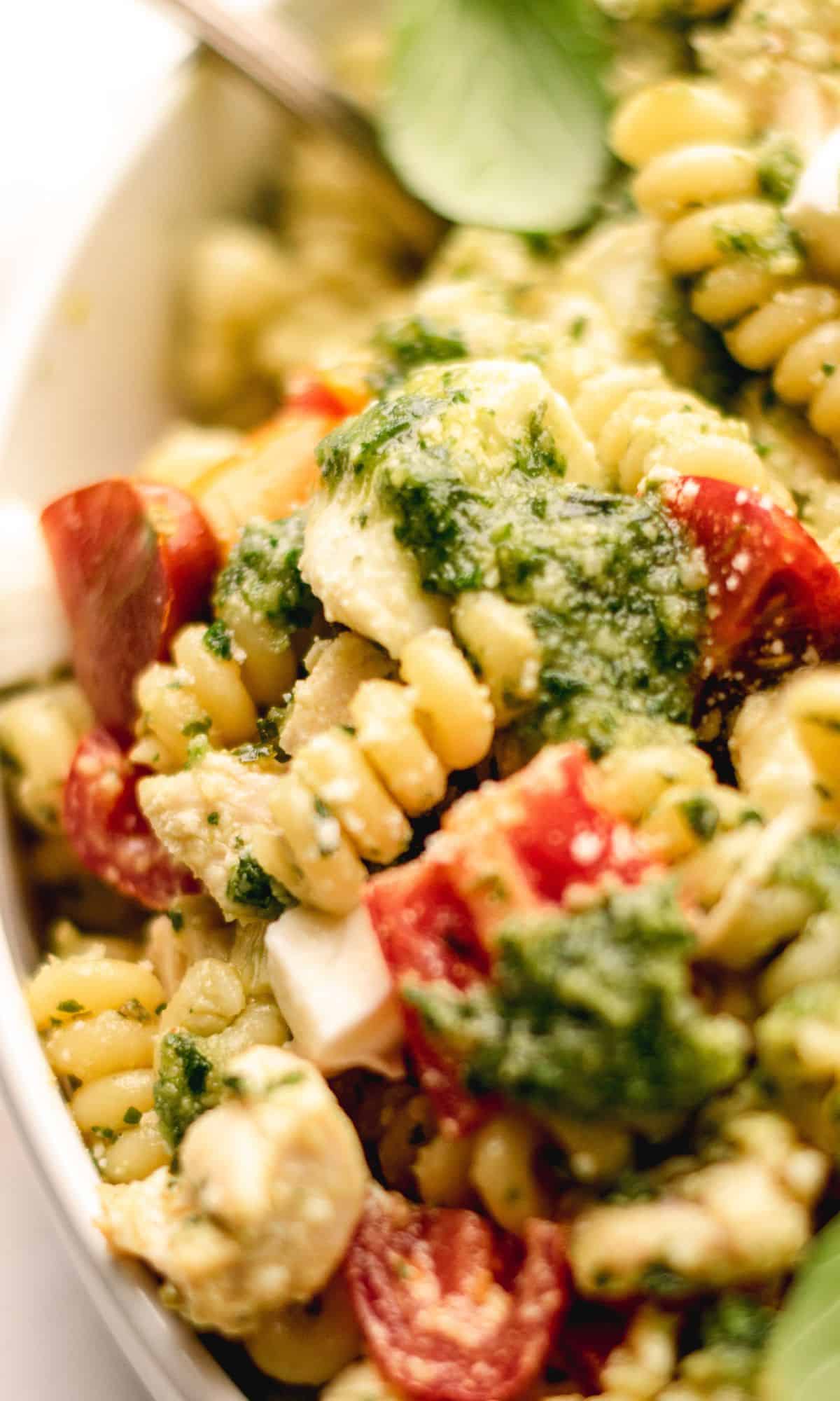 Pesto pasta salad topped with basil leaves in a white bowl.