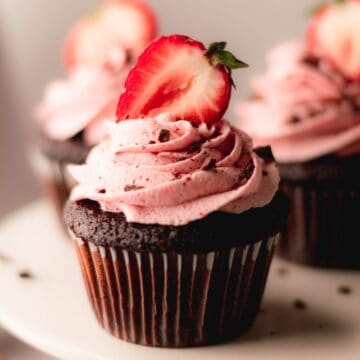 Chocolate cupcakes with strawberry buttercream and a halved strawberry on top.