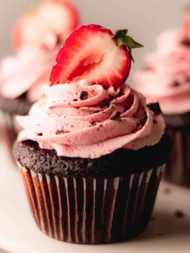 Chocolate cupcakes with strawberry buttercream and a halved strawberry on top.