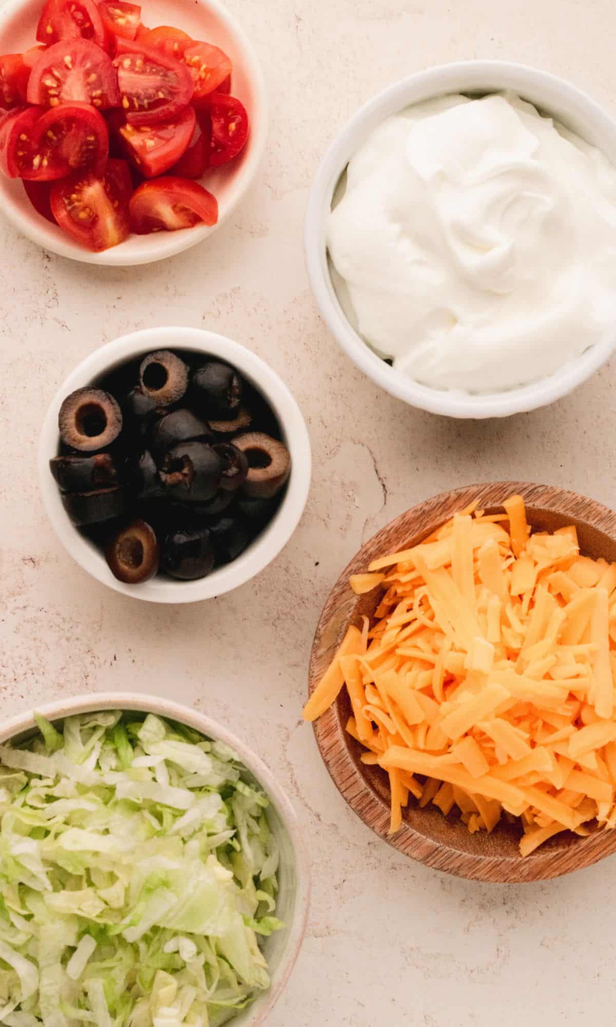 Taco cup toppings ingredients in varying bowl shapes and sizes.