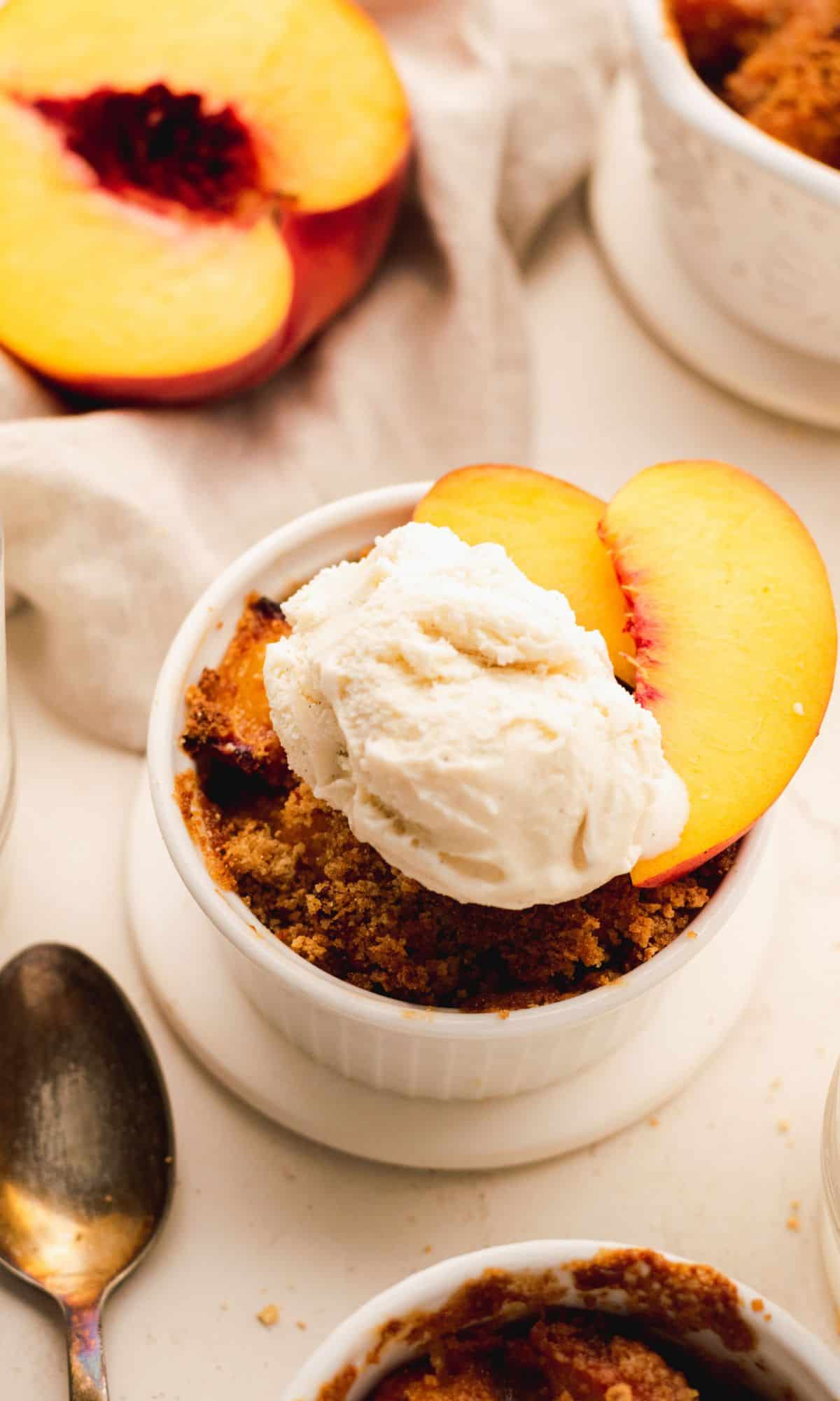 Air fryer peach crisp in a white ramekin topped with ice cream and peach slices.