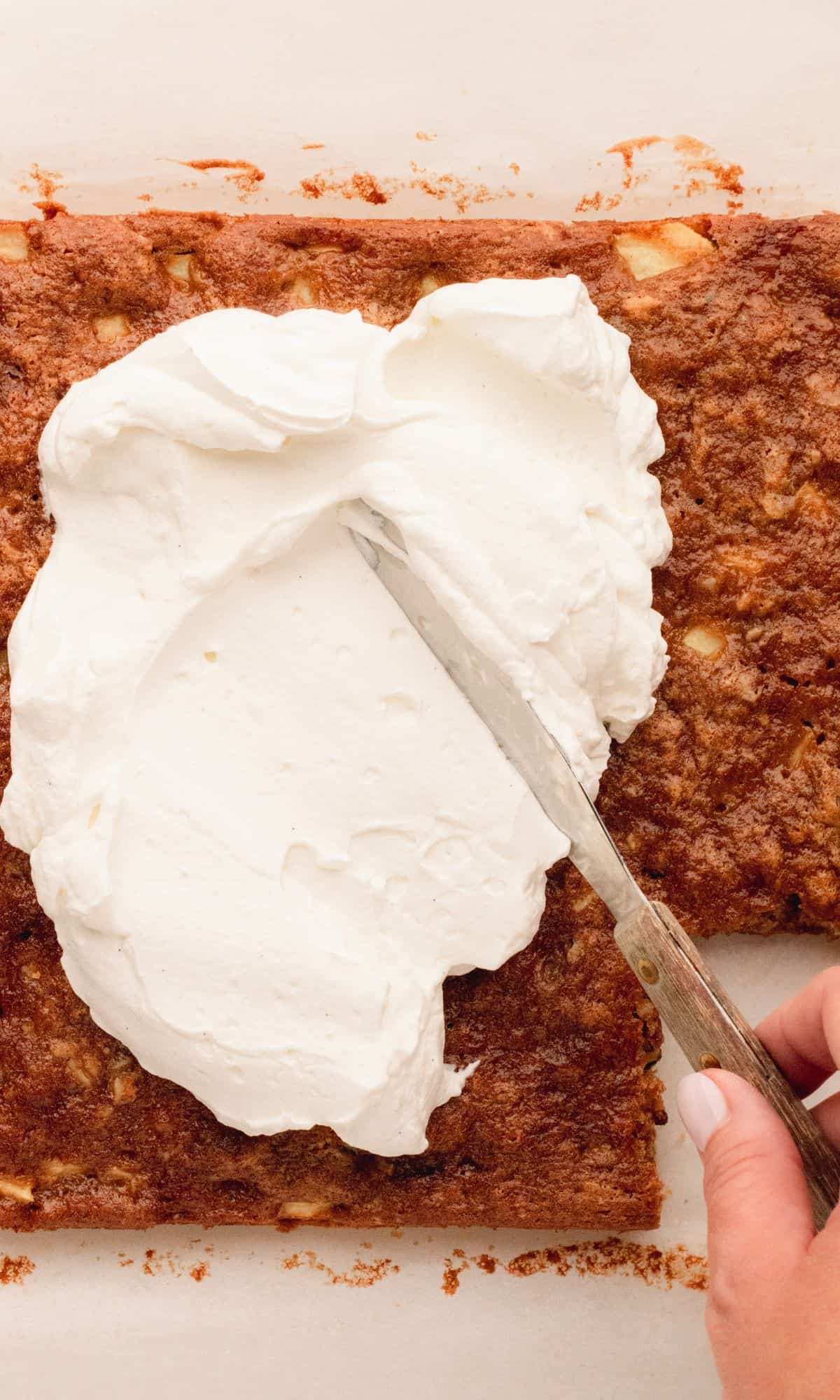 Whipped cream topping getting spread on sour cream apple bars.