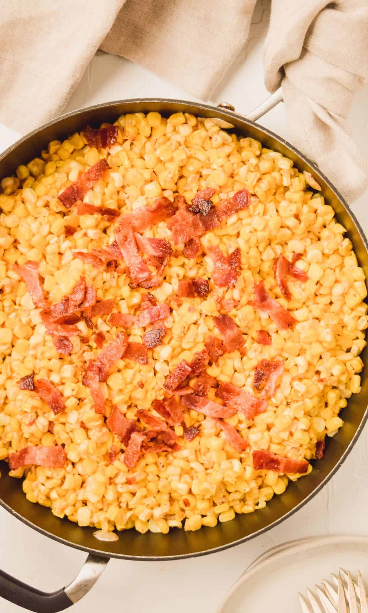 Creamy skillet corn in a skillet topped with bacon.