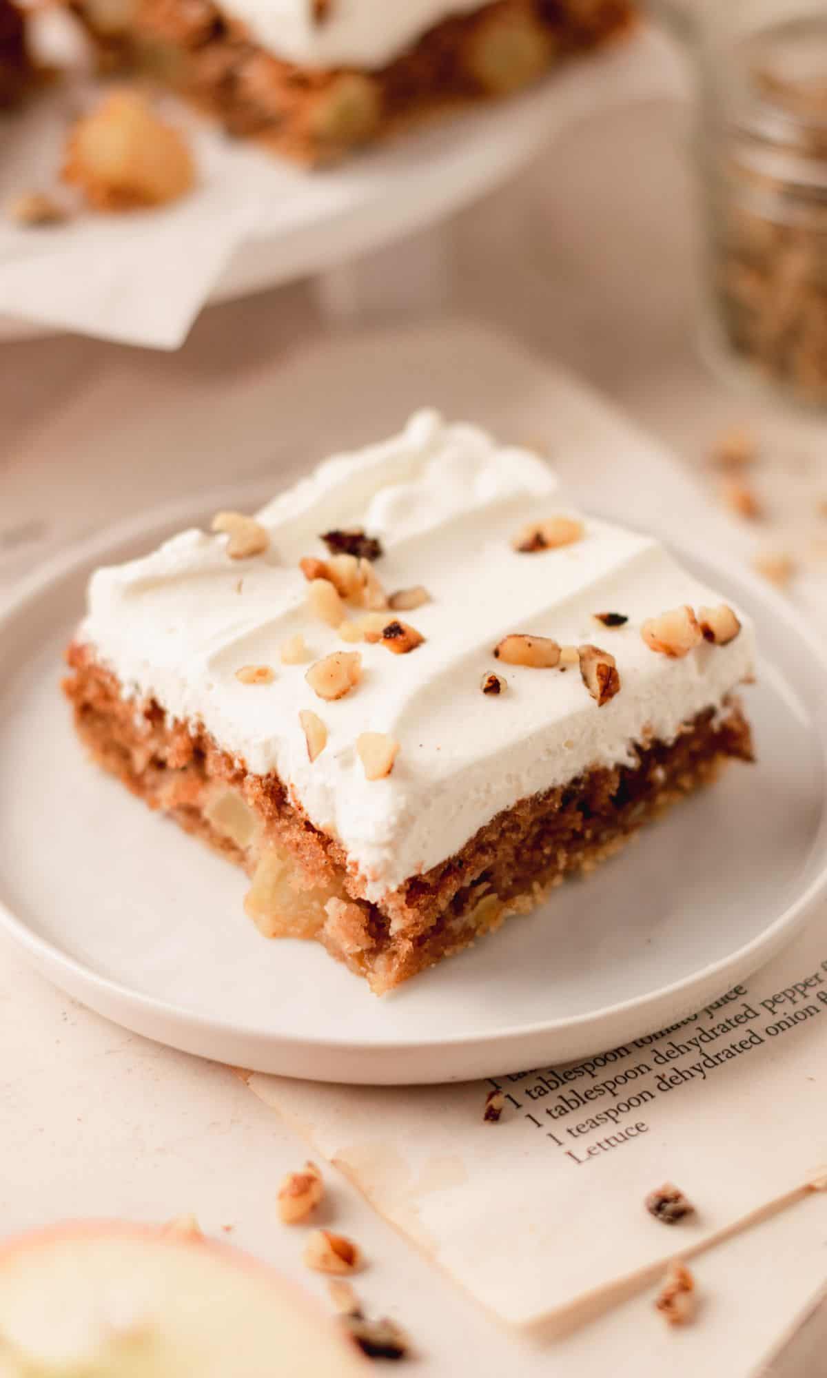 Sour cream apple bar topped with whipped cream and walnuts on a white plate.