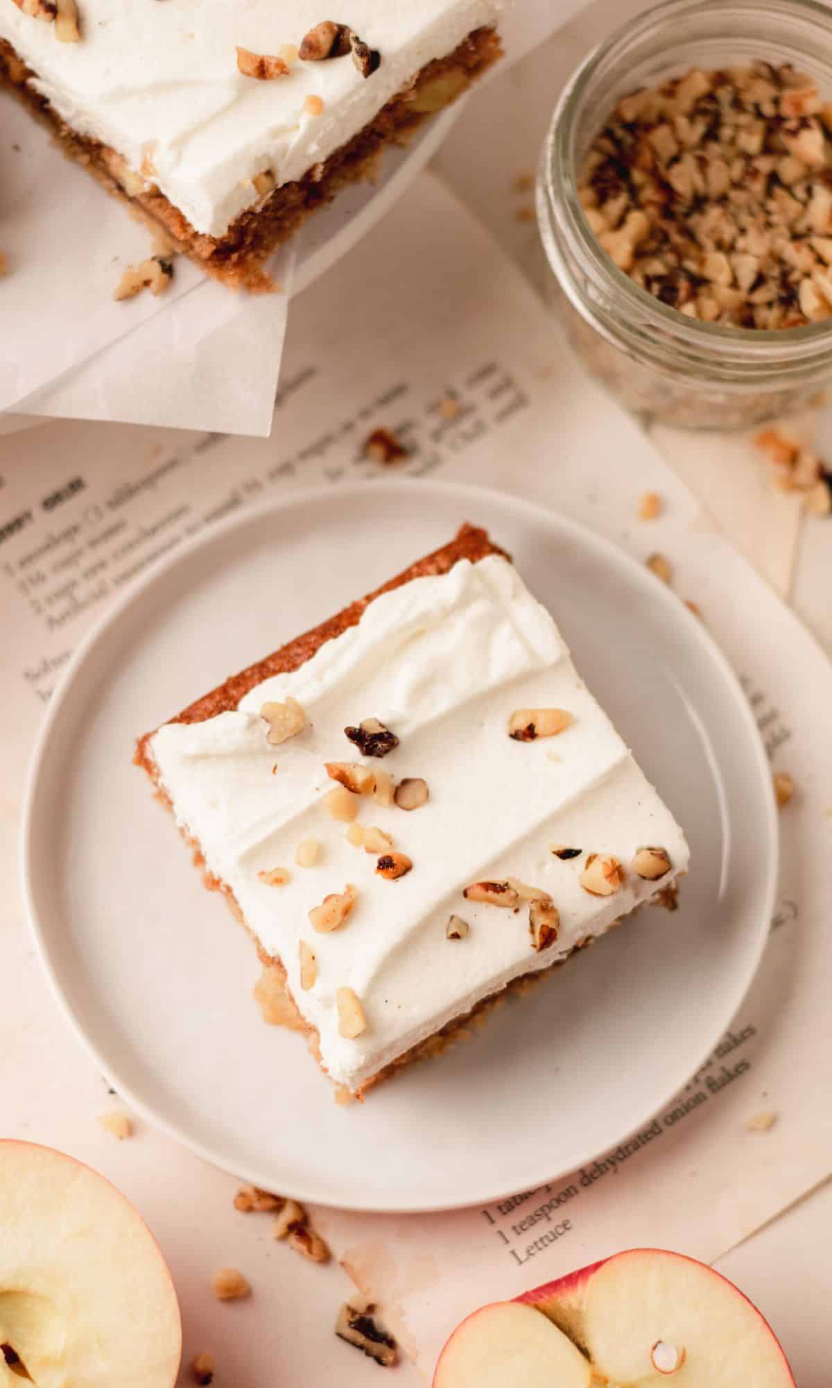 Sour cream apple bar topped with whipped cream and walnuts on a white plate.