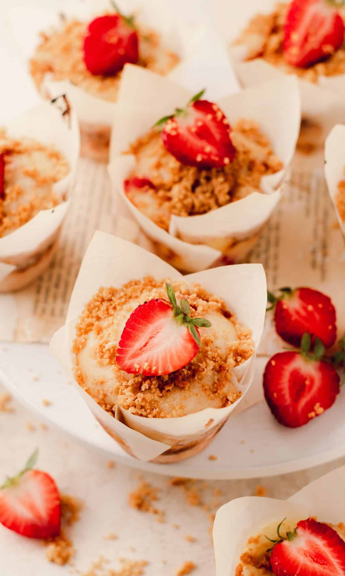 A strawberry cheesecake muffins in a white parchment paper liner topped with a strawberry.