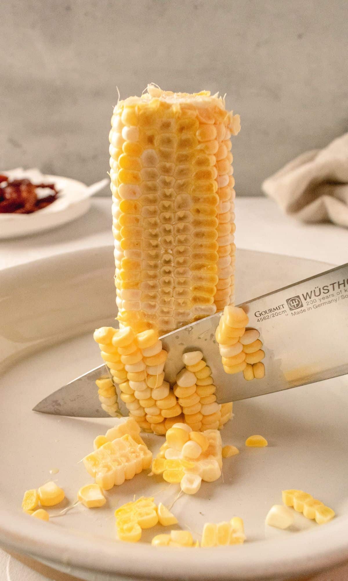 Cutting corn off of a corn cob with a large knife.