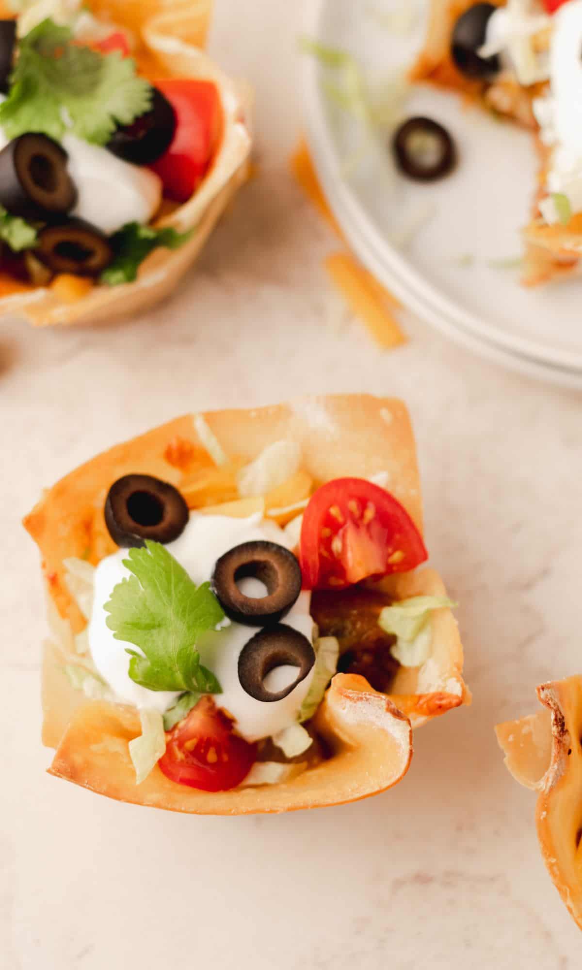 Double layer beef taco cups toped with sour cream, black olives, tomatoes, and cilantro.