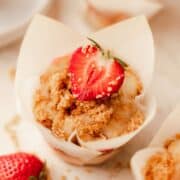 A strawberry cheesecake muffin in a white parchment paper liner topped with a strawberry.