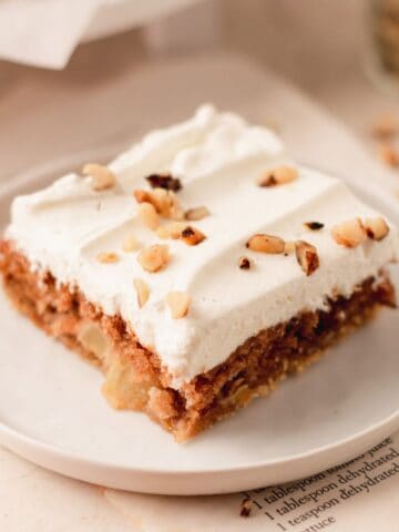 A sour cream apple slice bar topped with whipped cream and walnuts on a white plate.