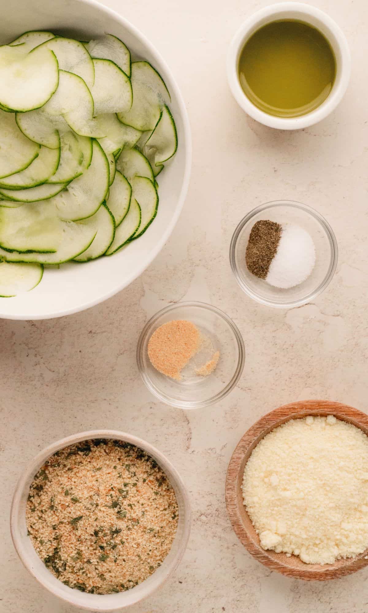 Zucchini chips ingredients in varying bowl shapes and sizes.