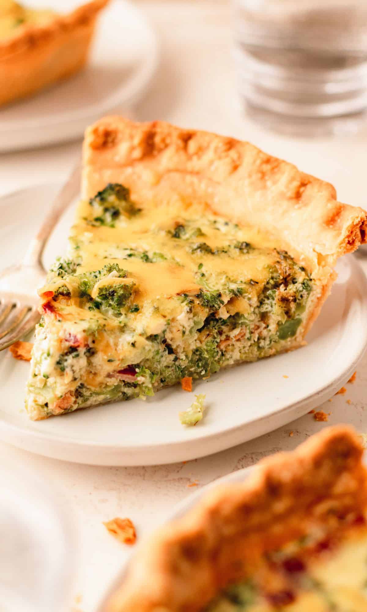 A slice of quiche on a white plate with a fork.
