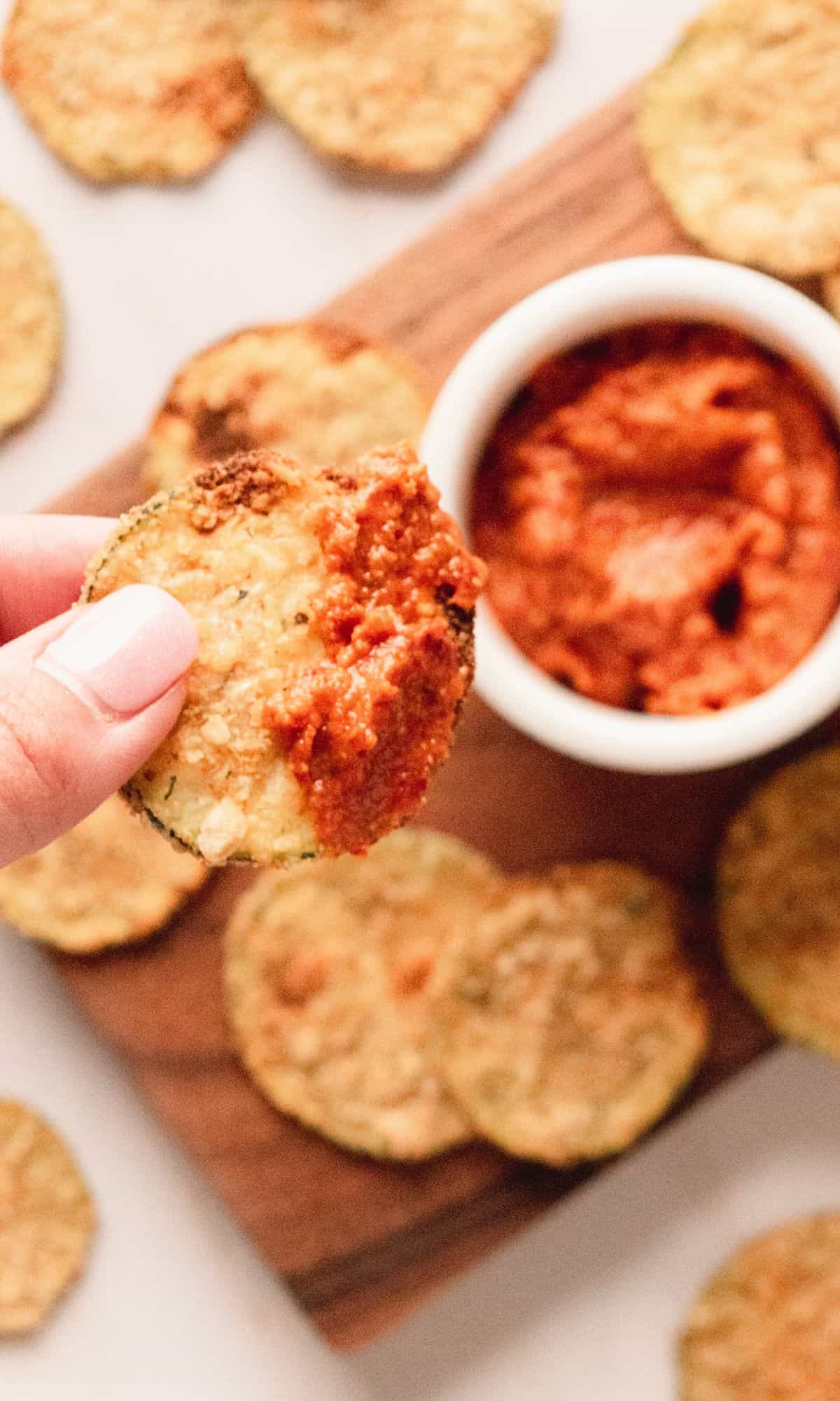 Close up shot of zucchini chip dipped in tomato sauce.