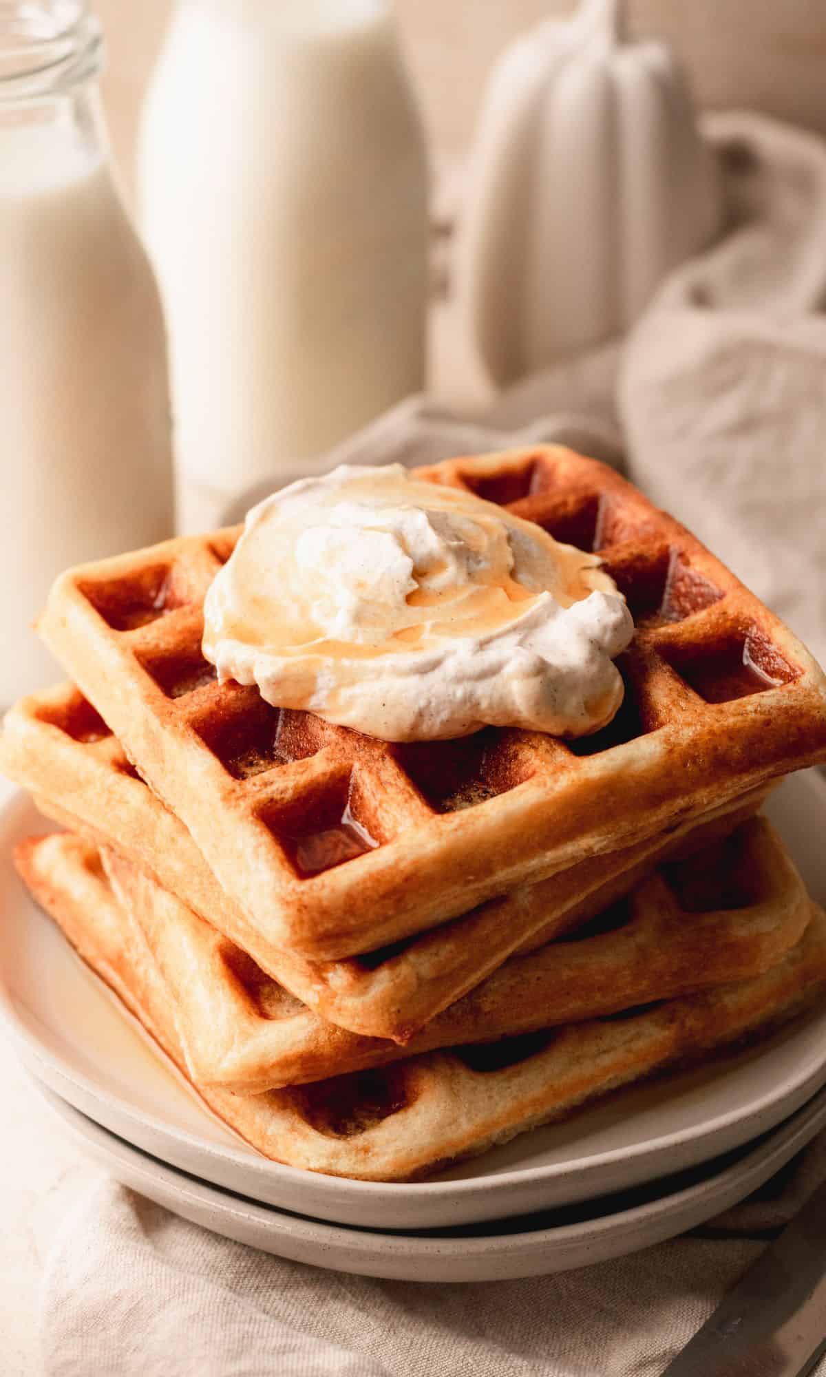 Belgian waffles topped with whipped cream on a white plate.