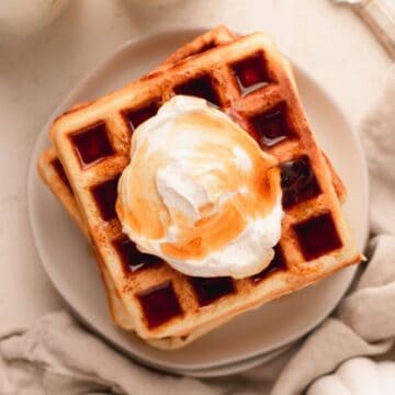 Belgian waffles topped with whipped cream on a white plate.