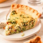 A slice of quiche on a white plate with a fork.